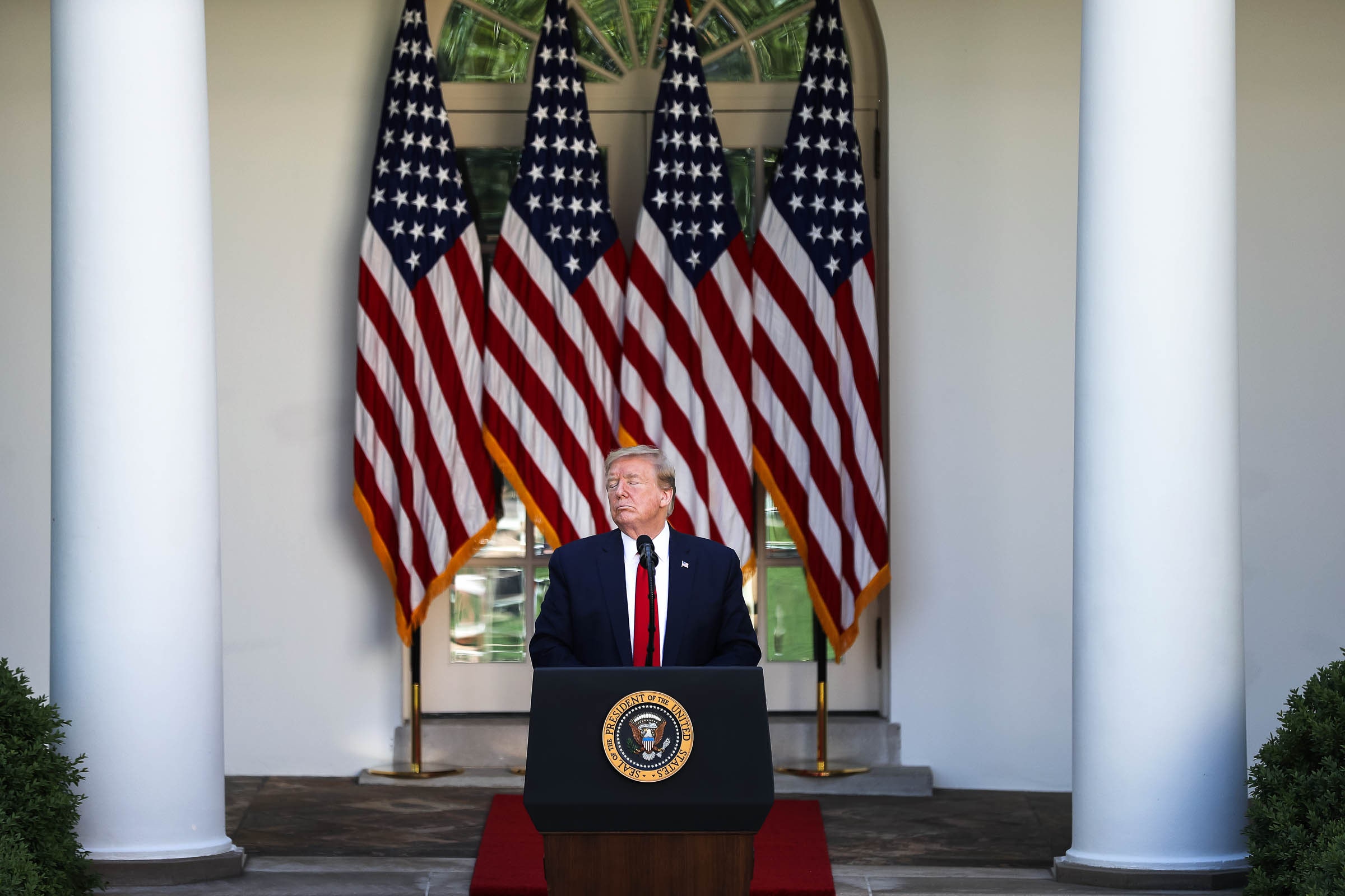 Trump na rostro perto da Casa Branca em frente a quatro bandeiras americanas