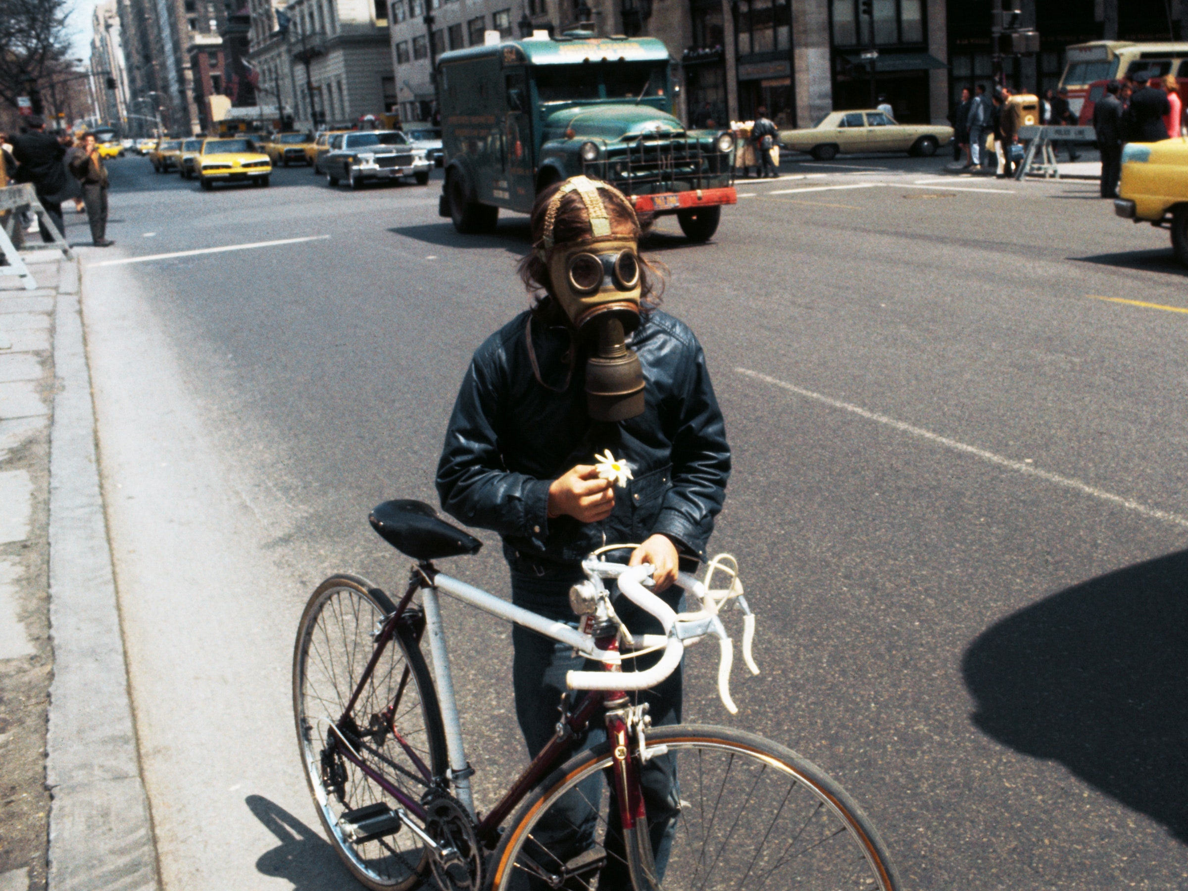 Um ciclista no dia da terra em 1970 em uma máscara de gás segurando uma flor