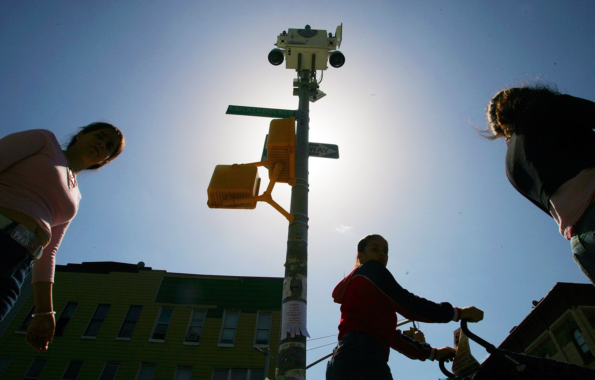 Pedestres caminham sob câmeras sem fio do Departamento de Polícia de Nova York presas a um poste de luz.