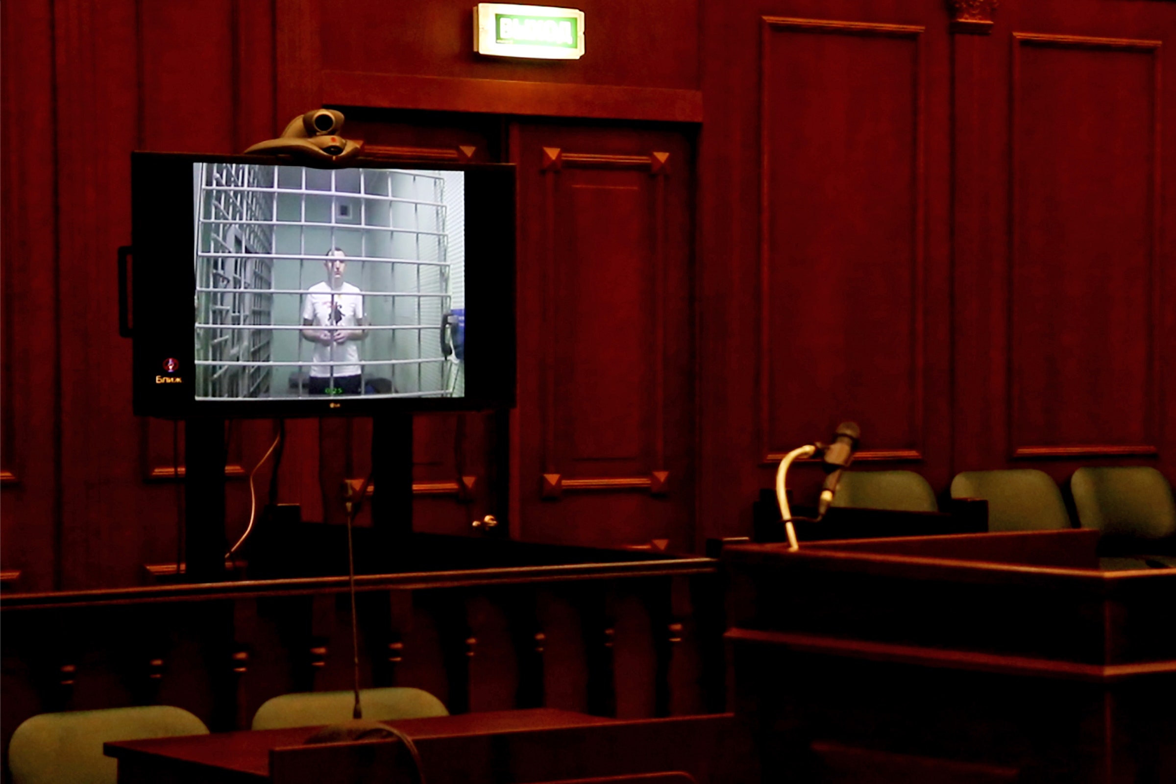 A tela instalada no tribunal e mostrando o prisioneiro