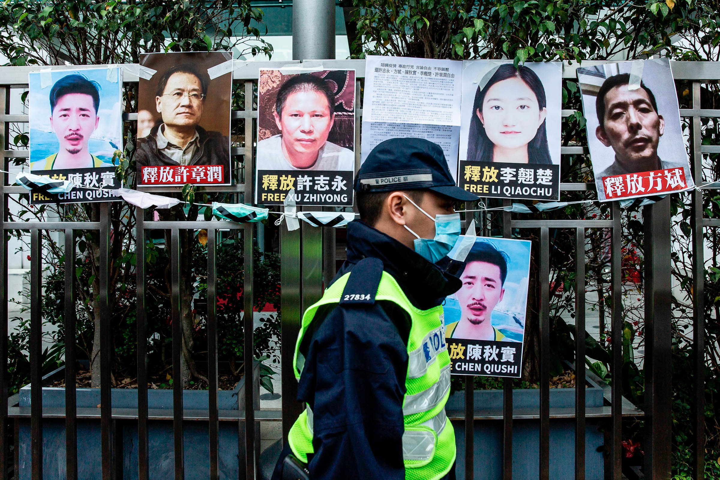 Um policial passa por cartazes de ativistas de direitos humanos detidos colados em uma cerca em Hong Kong.
