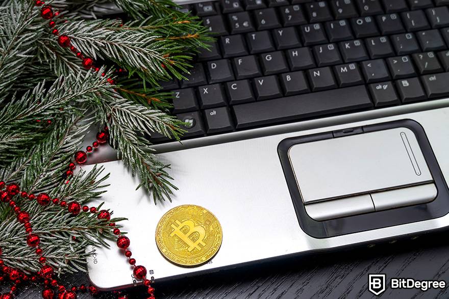 Compre cartõe s-presente com criptomoeda: Bitcoin físico está em um laptop ao lado de um ramo de abeto decorado.