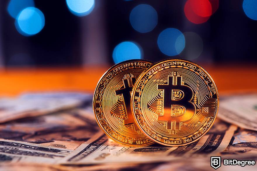 Como investir em criptomoeda: duas moedas físicas de Bitcoin são colocadas em uma pilha de notas de dólar.