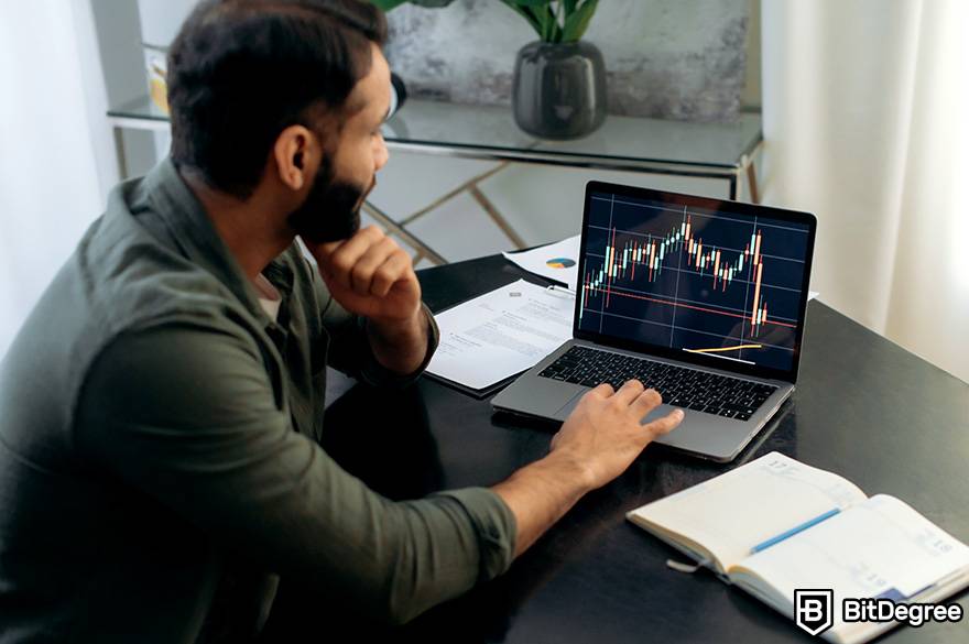 Como investir em criptomoeda: um homem olha para um laptop no qual o volume do mercado é exibido.