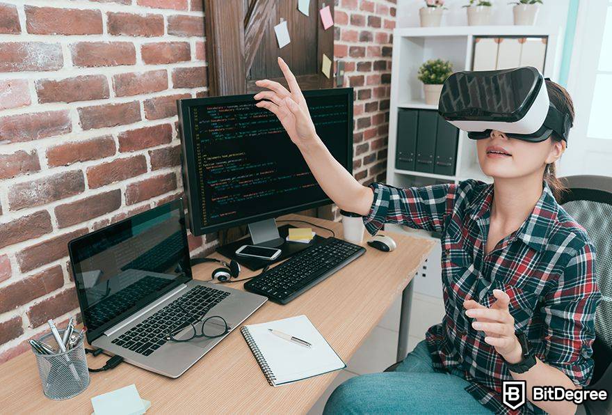 Leis de Metavselnaya: Uma mulher usa VR ao lado de um computador ao programar.