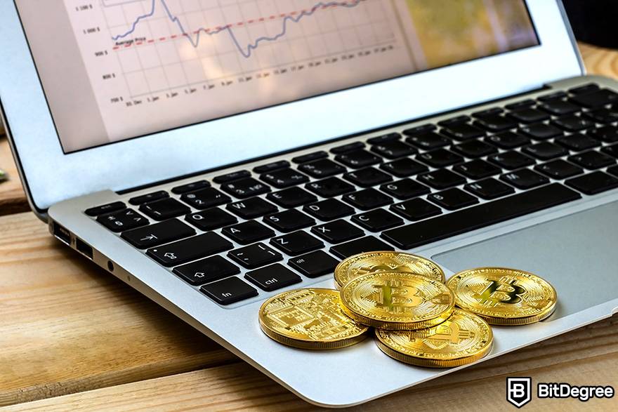 O que é Fiat em criptomoeda: moedas físicas de bitcoin em frente ao laptop, que exibe dados de mercado.