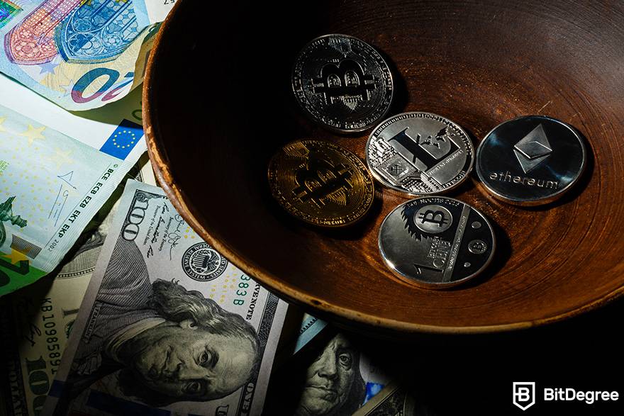 O que é negociação à vista de criptomoedas: Uma tigela contendo cinco moedas de criptomoeda fica ao lado de várias notas de moeda fiduciária.