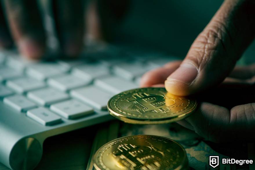 O que é Washing Trading Crypto: Uma pessoa que segura uma moeda física BTC perto do teclado.